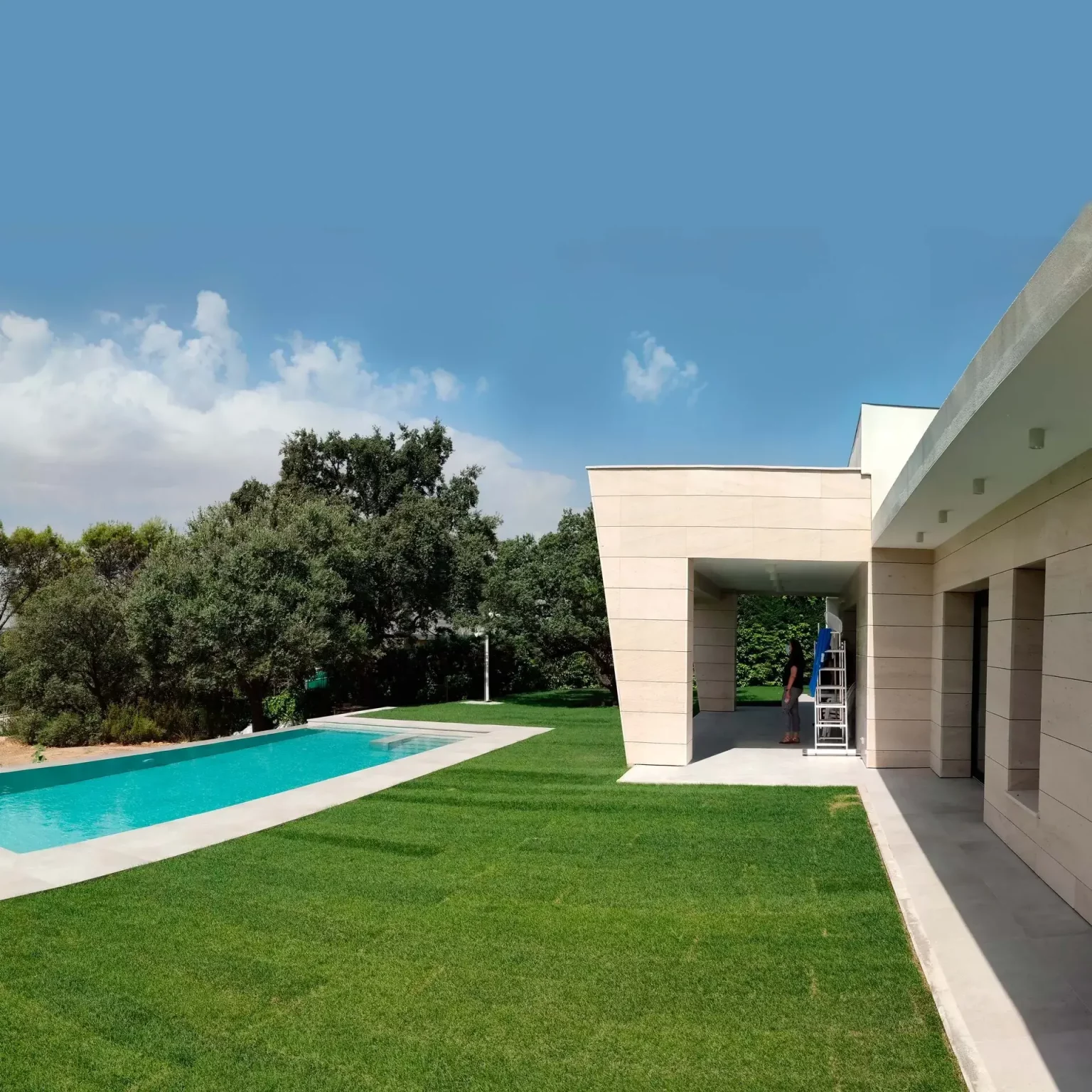 Vista del jardín lateral con césped natural y piscina integrada bajo el porche de la Villa E82.