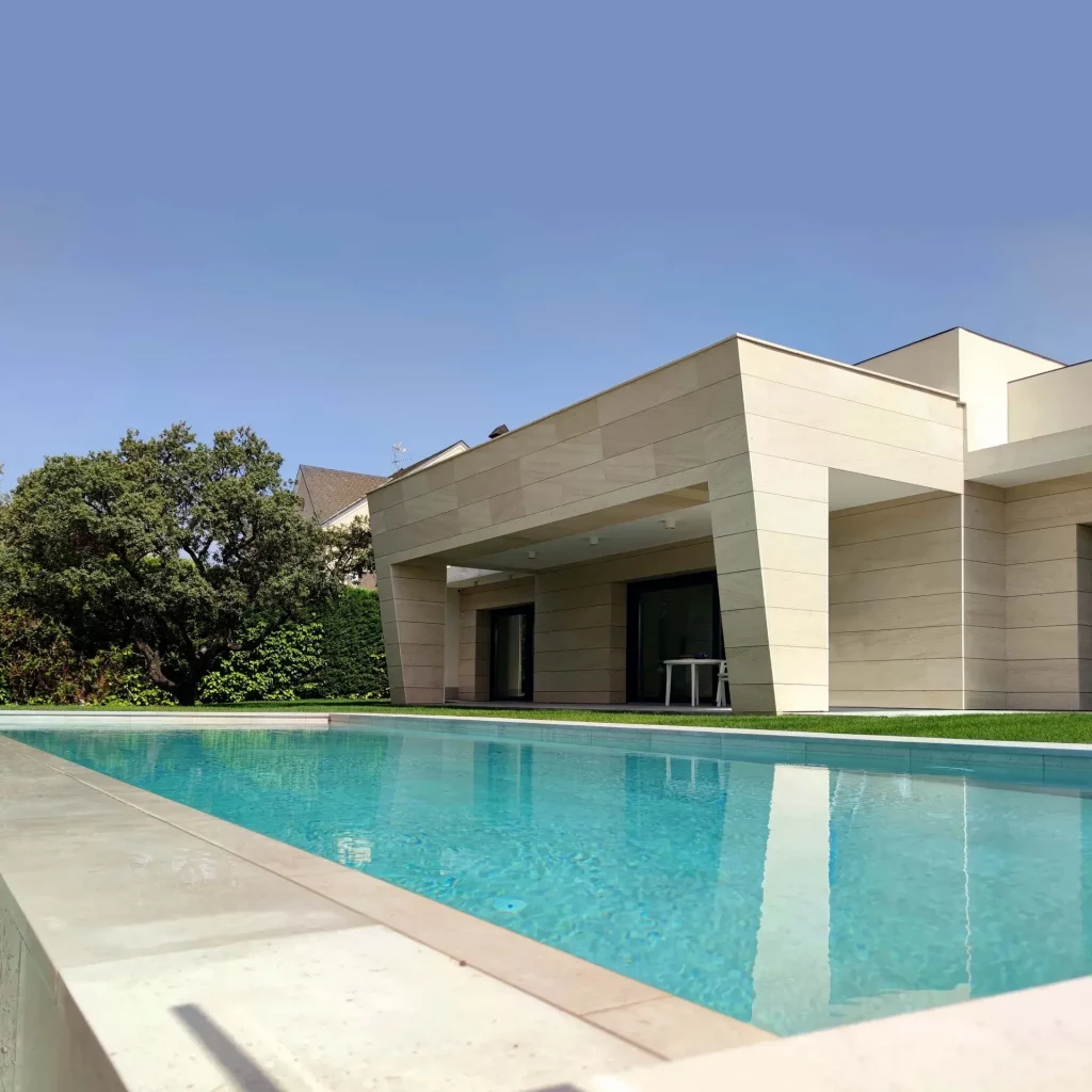Vista del jardín lateral con césped natural y piscina integrada bajo el porche de vivienda unifamiliar en majadahonda de la Villa E82.