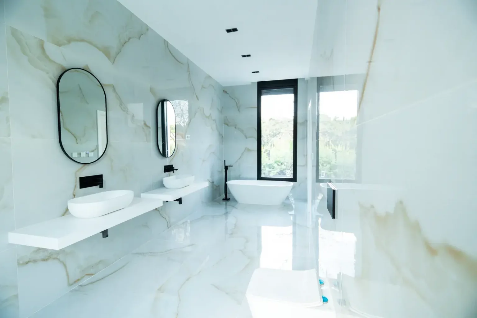 Baño principal moderno con revestimiento de mármol blanco, lavabo doble y bañera exenta en Villa IL3
