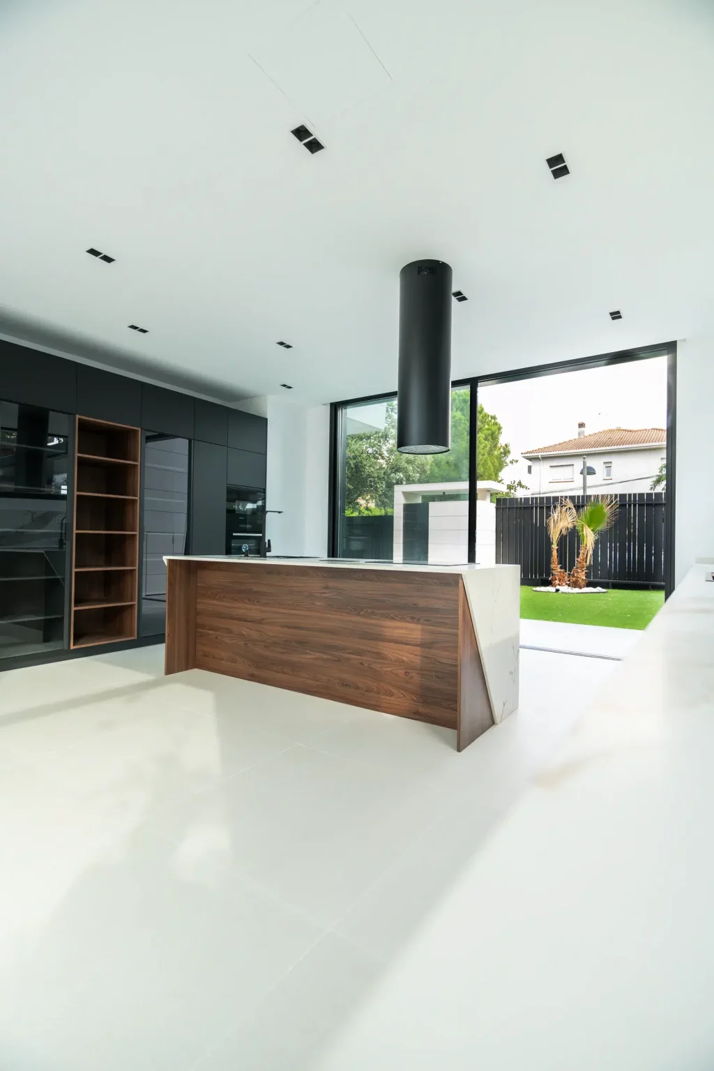 Cocina abierta de diseño minimalista con isla central de madera y campana cilíndrica negra en Villa IL3