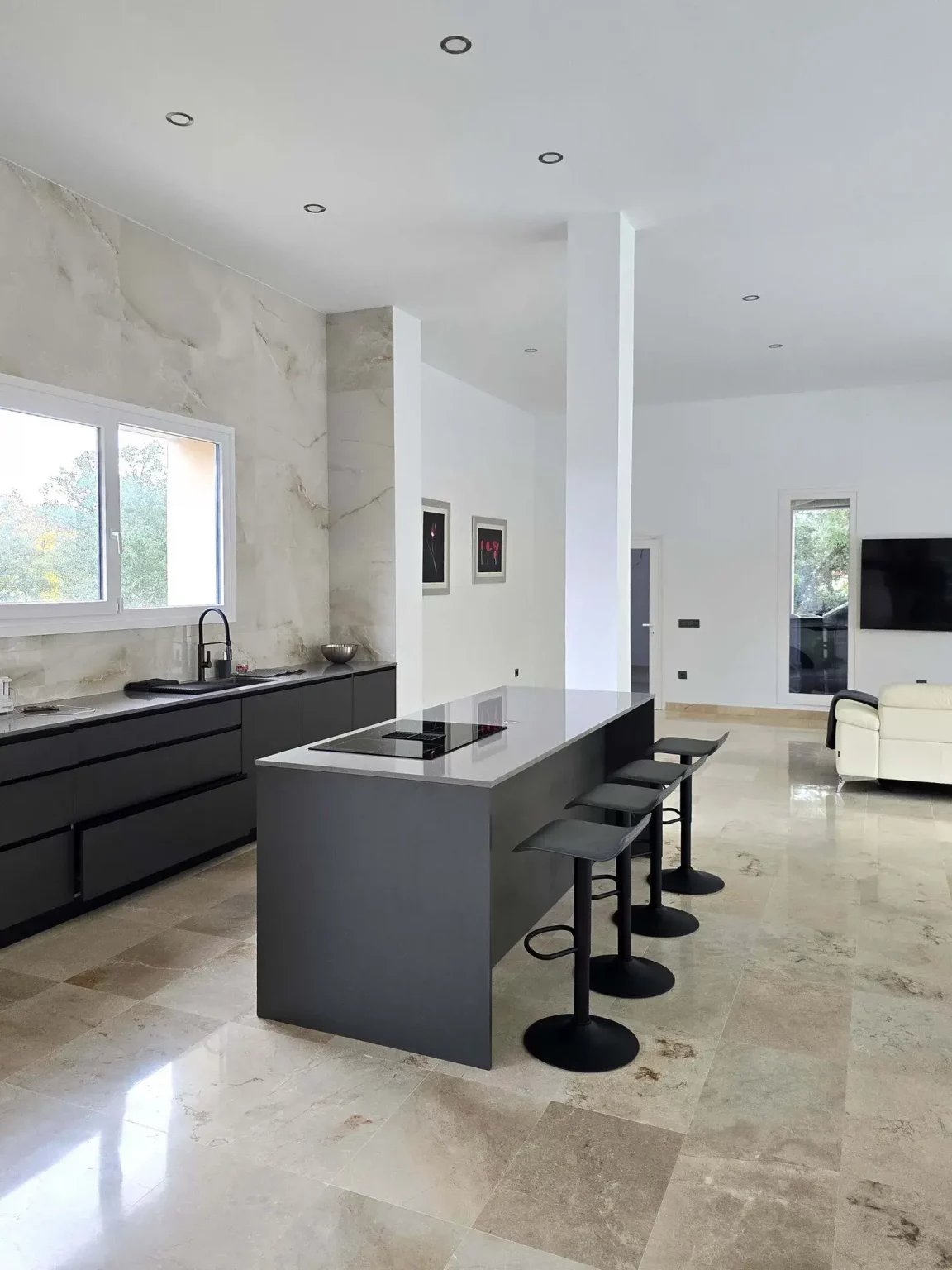 Cocina moderna de concepto abierto con una gran isla central negra, taburetes y suelos pulidos de gran formato.