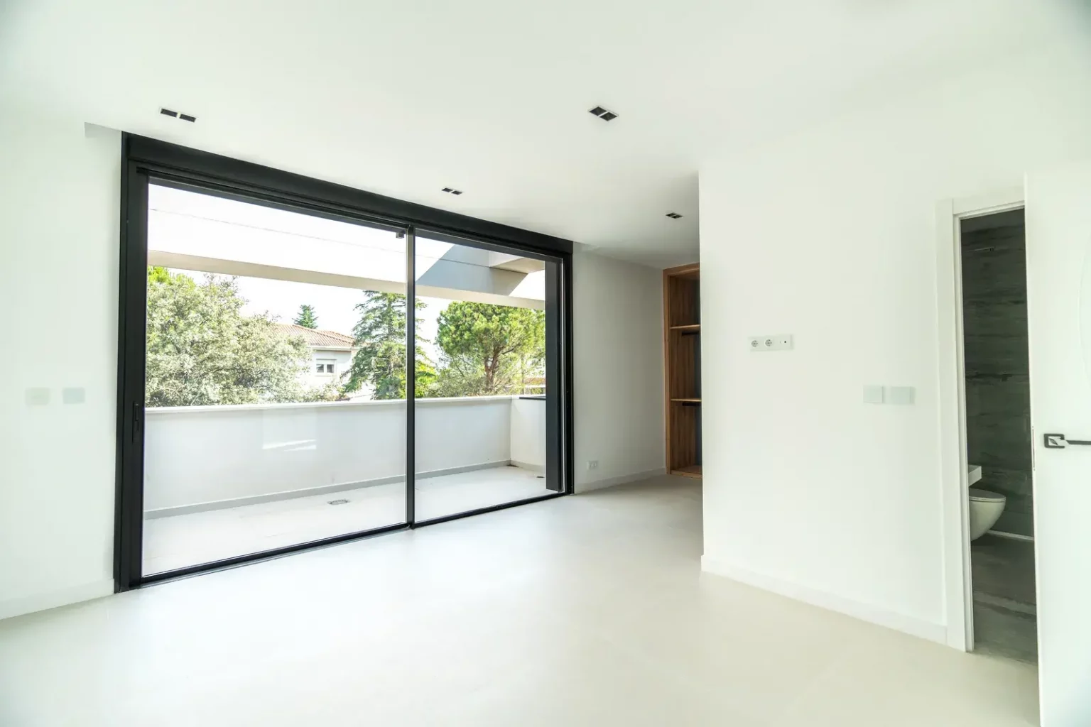 Dormitorio principal en suite con grandes ventanales, balcón y baño integrado de diseño moderno en Villa IL3