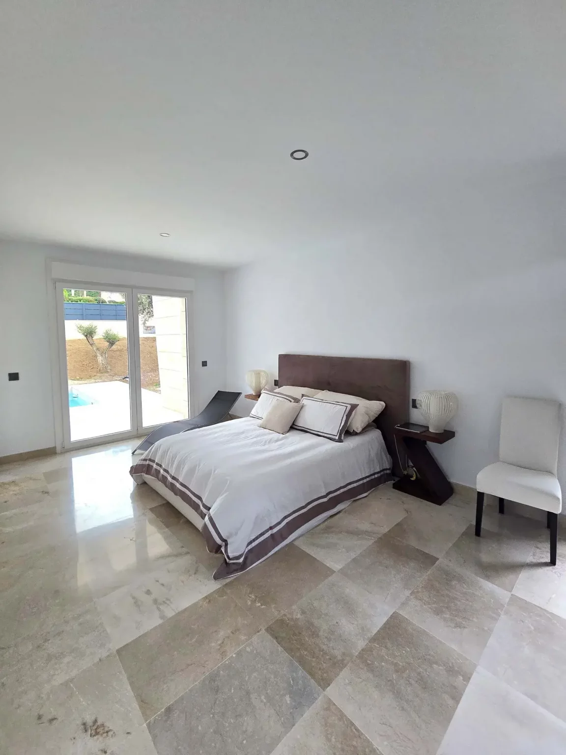 Dormitorio principal de diseño contemporáneo con cama de matrimonio, suelos de piedra y decoración neutra.