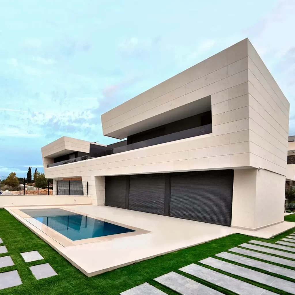 Obra terminada de una vivienda unifamiliar en Boadilla del Monte, mostrando la fachada de piedra natural, la piscina y el jardín lateral.